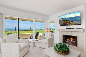 A modern living room with a large TV, comfortable seating, a fireplace, and a view of the ocean. - Sunset Retreat-Gorgeous! Oceanfront Luxury-Del Mar Fairgrounds, Pool, Beach (Solana Beach)