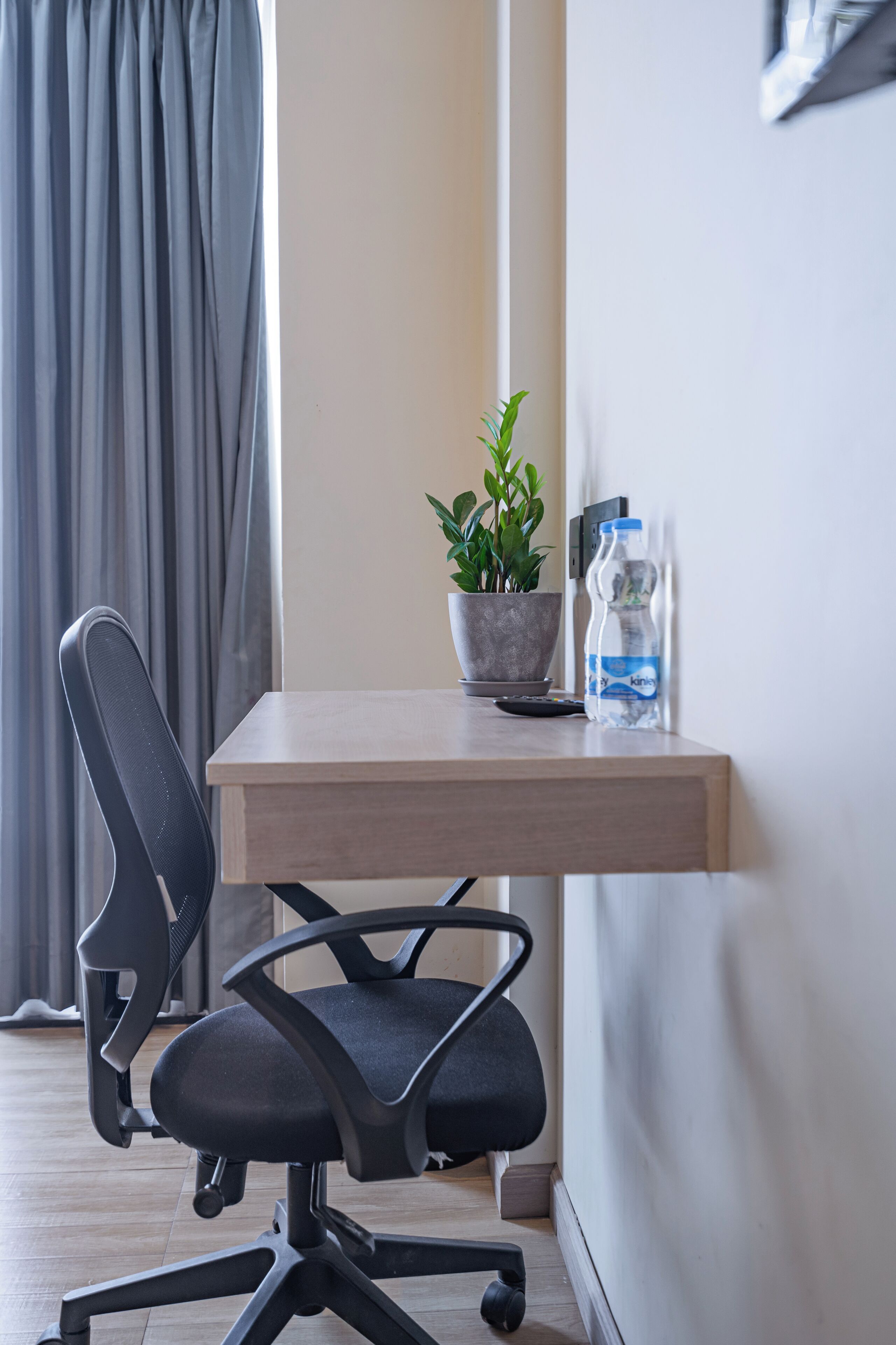 Una silla de oficina moderna, un pequeño escritorio con una planta en maceta, una botella de agua y un control remoto.
