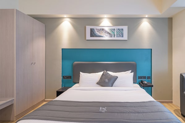 A hotel room with a bed, a wardrobe, a nightstand, a phone, and a painting on the wall.