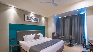 A modern hotel room with a large bed, a teal accent wall, a ceiling fan, a desk with a chair, and a window with curtains. - Republic Inn (Tirupati)