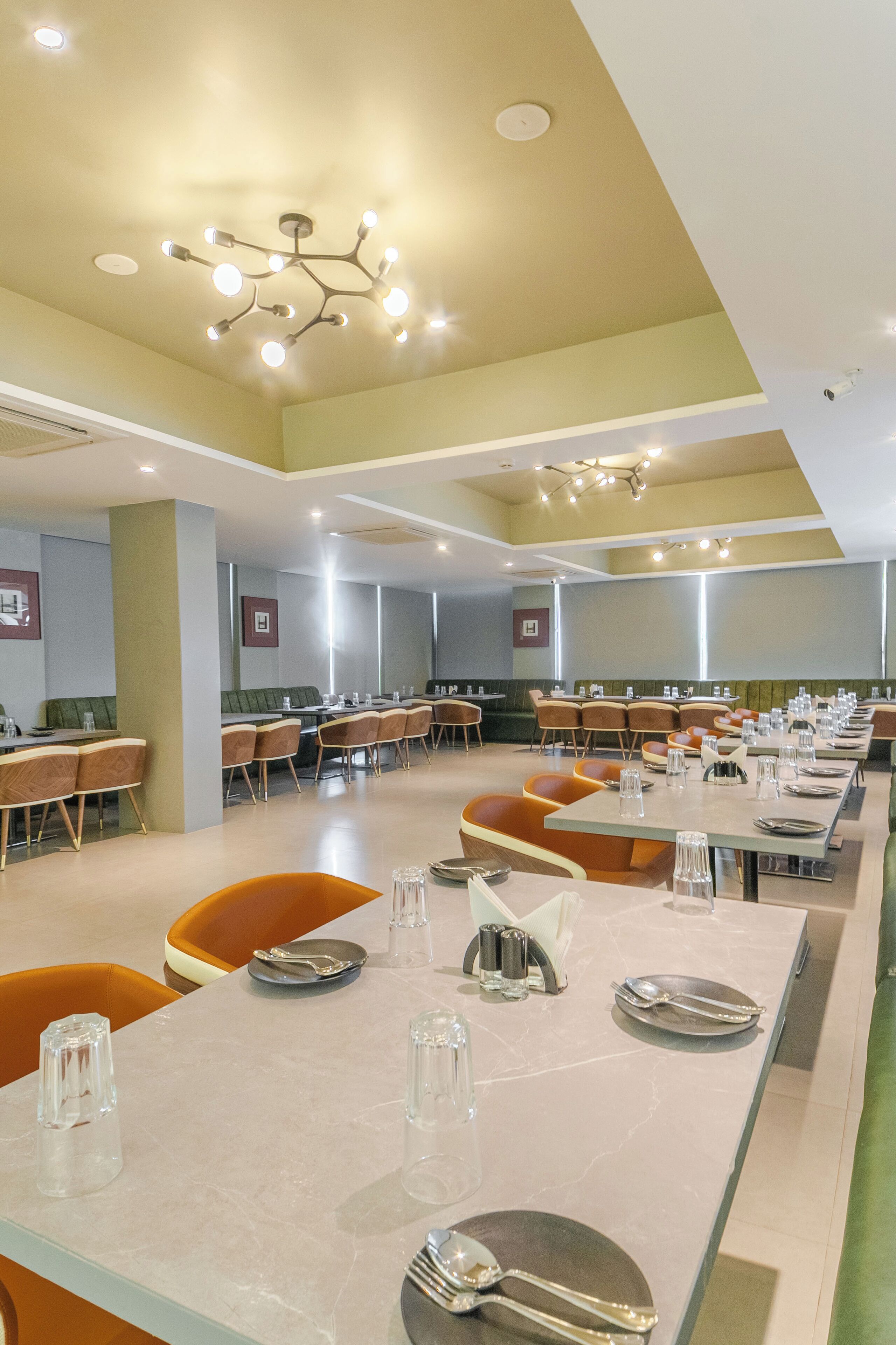 Uma sala de jantar ampla com várias mesas e cadeiras, um lustre moderno e quadros nas paredes.