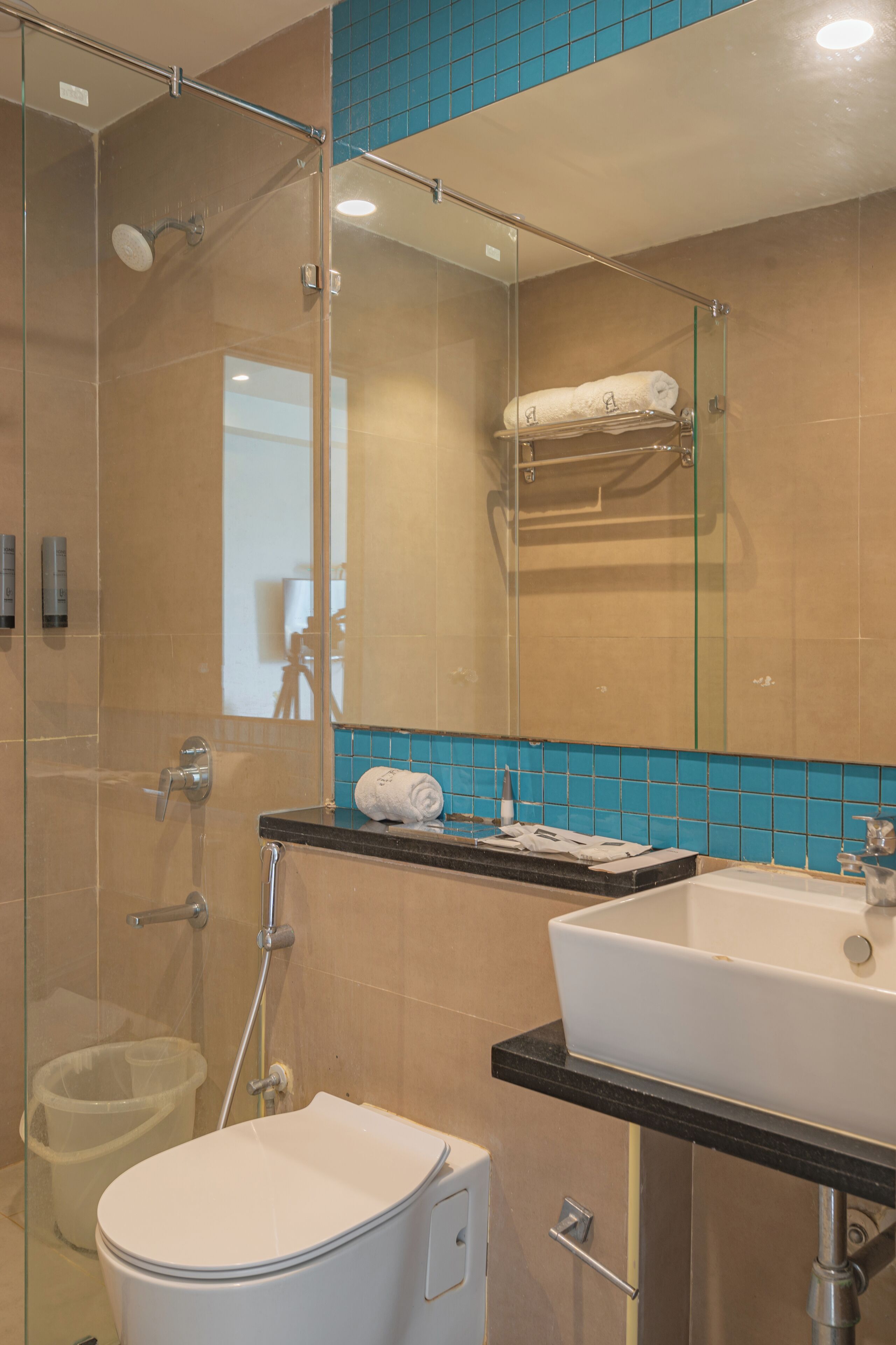 Et moderne badeværelse med en glasbrusekabine, et hvidt toilet, en vask med sort bordplade og en backsplash med blå fliser.