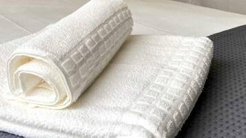 A neatly made bed with white linens and a rolled towel on the bed.