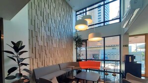 Et moderne interiør med en hjørnesofa, et lille bord og stole. Væggen er dekoreret med geometriske mønstre, og et stort vindue giver udsigt ud.