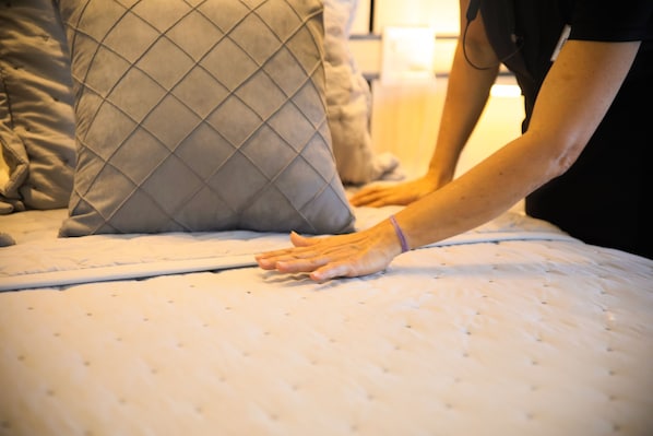 Eine Hand richtet eine Matratze auf einem Bett mit einem gesteppten Kopfkissen.
