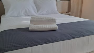 A neatly made bed with white linens and a gray blanket, a wooden headboard, and a bedside table with a lamp.