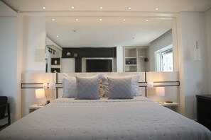 A modern hotel room with a large bed, two bedside tables with lamps, a wardrobe, and a mirror above the bed.