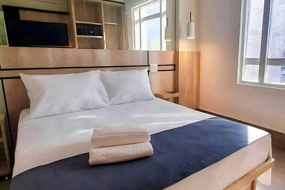 A modern hotel room with a large bed, built-in storage, and large windows.