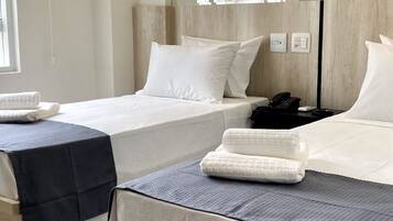 A hotel room with two beds, a large mirror, a wooden headboard, a bedside table with a phone, and a window with a view of buildings.
