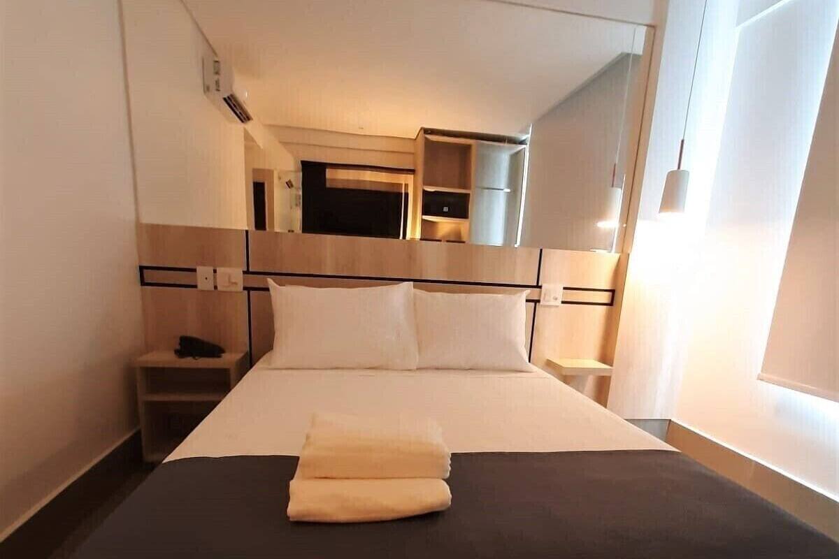 A hotel room with a bed, bedside tables, a mirror, and a built-in TV.