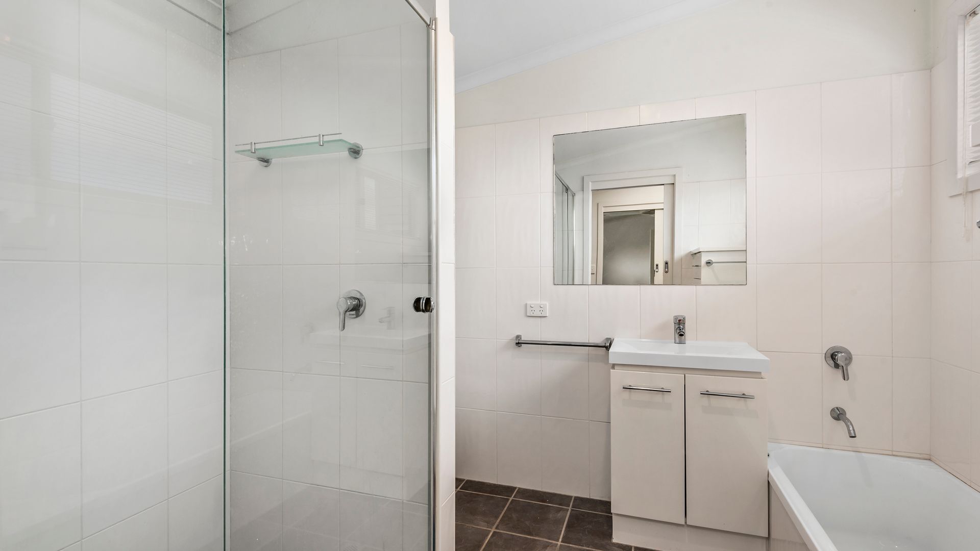 A modern bathroom with a glass shower enclosure, a white sink with a mirror above, and a bathtub.