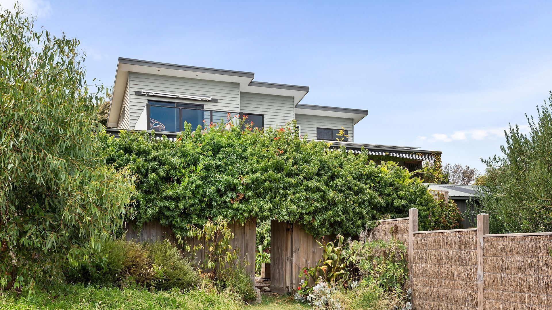Une maison à deux étages dotée d’un patio couvert et d’une clôture en bois.