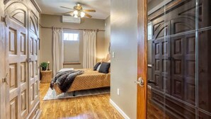 A bedroom with a bed, a ceiling fan, a window with curtains, and a wooden floor. - Aces & Eights - Downtown Sturgis with garage! (Sturgis)