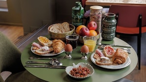 Una mesa de desayuno con croissants, huevos, pan, frutas y bebidas.