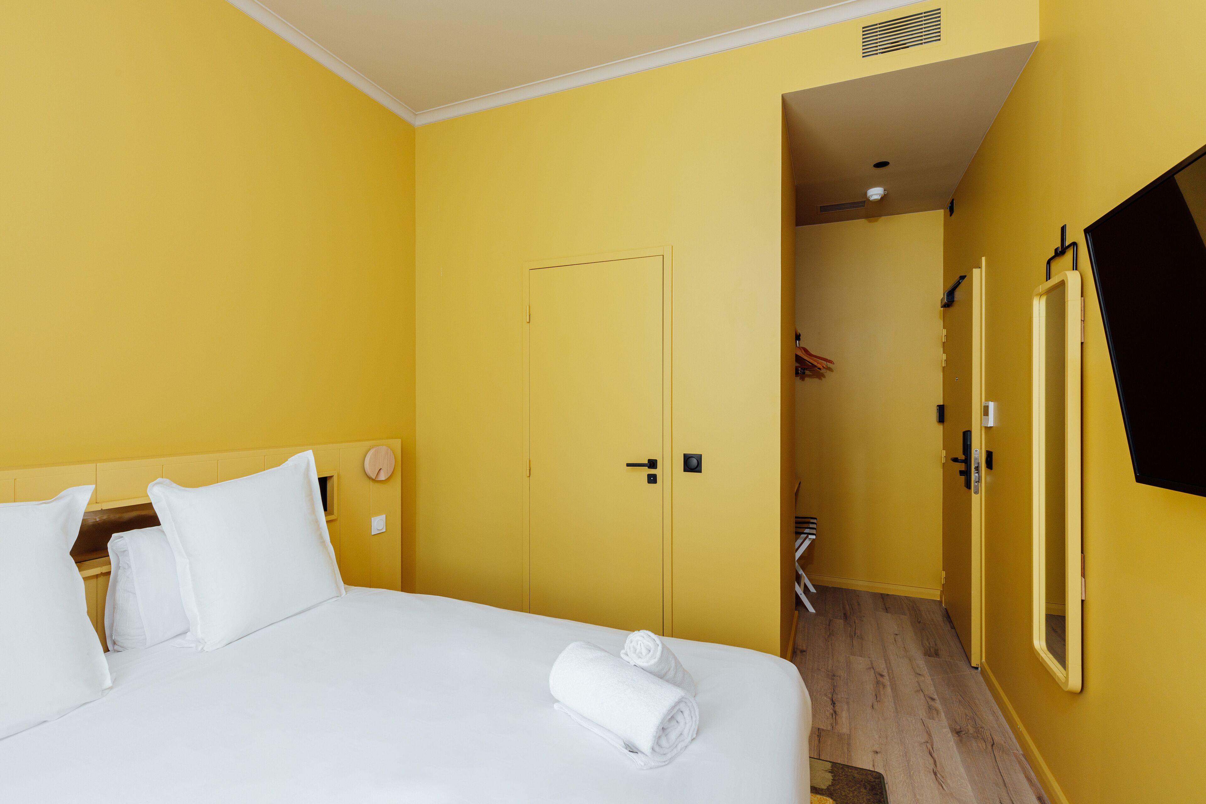 A hotel room with a bed, a door, and a mirror on the wall.