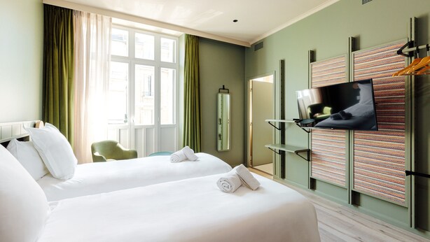 Habitación de hotel con dos camas, televisión, espejo y ventana con cortinas.