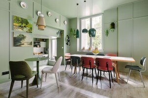 A dining area with a wooden table and chairs, a green wall with artwork, and pendant lights.