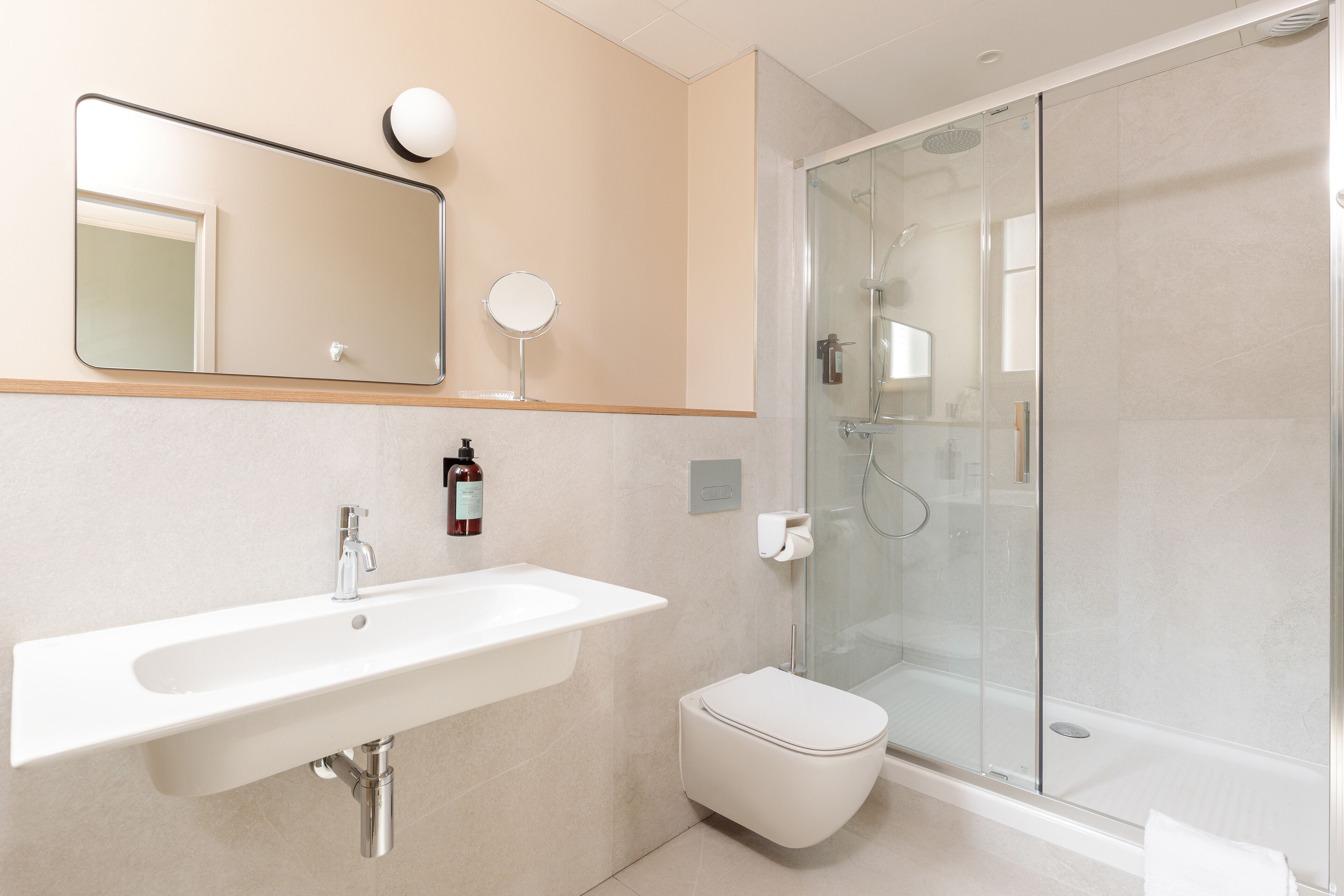 Een moderne badkamer met een wit wastafelmeubel, spiegel en toilet, en een douchecabine met glazen wanden.