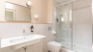 Een moderne badkamer met een wit wastafelmeubel, spiegel en toilet, en een douchecabine met glazen wanden.