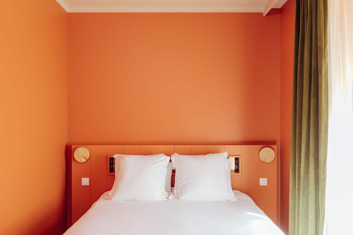 Ein ordentlich bezogenes Bett in einem Zimmer mit orangefarbenen Wänden und einem h ölzernen Kopfende.