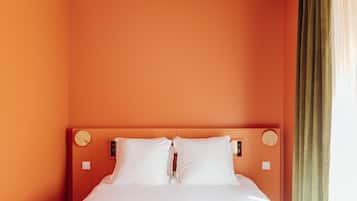 Een net opgemaakt bed in een kamer met oranje wanden en een houten hoofdbord.