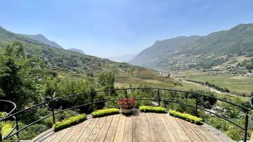 A wooden deck with a view of terraced fields and mountains.