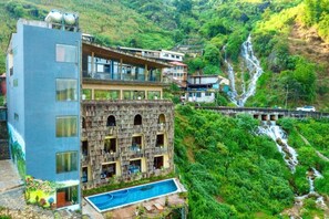 A multi-story hotel with a pool, set against a lush green hillside with a waterfall. - ARISTA HOMESTAY SAPA (Sa Pa)