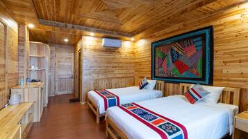 A wooden cabin with two beds, a kitchen area, and a large quilted artwork on the wall.