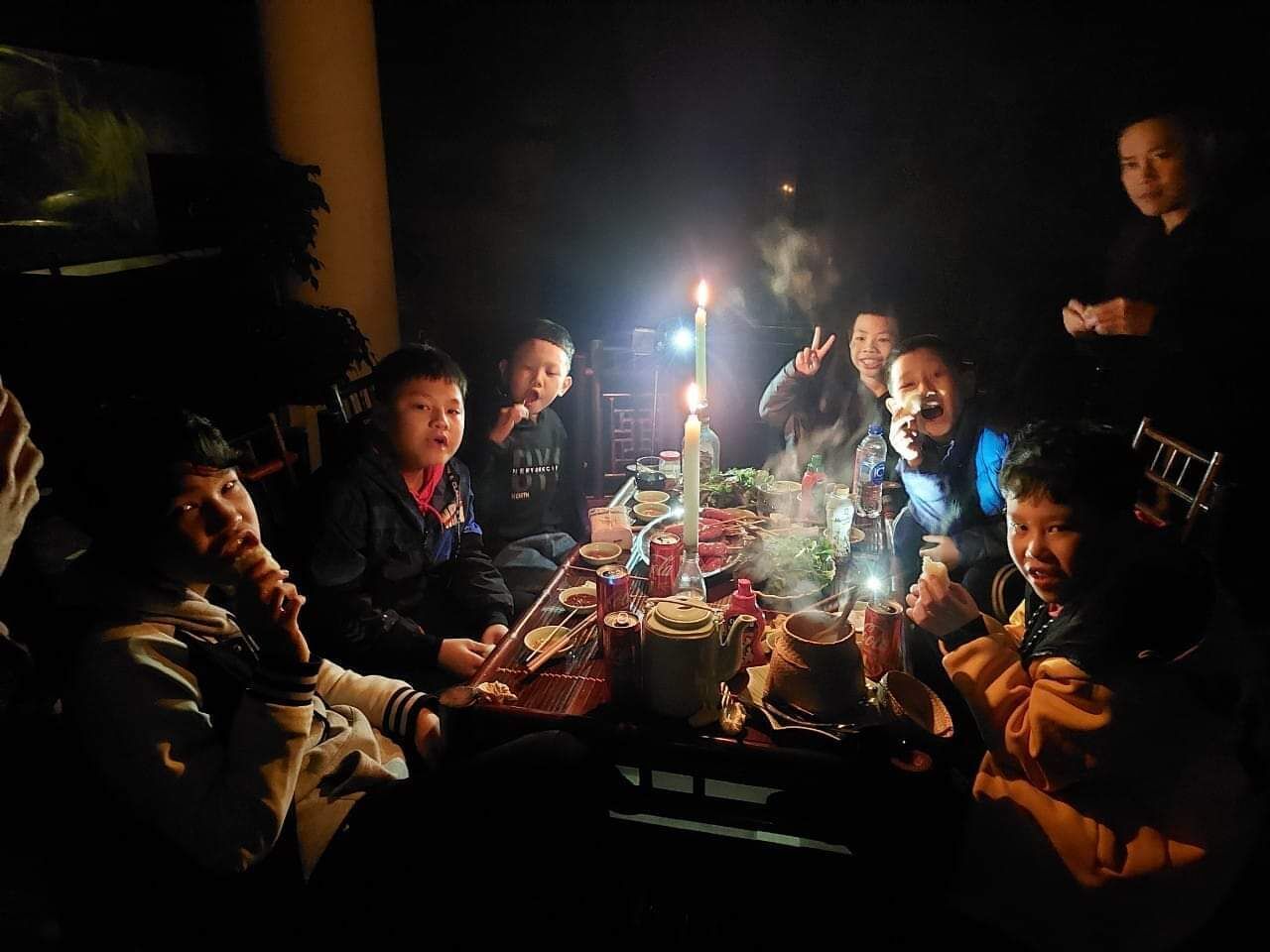 A group of people around a table with a lit candle, various dishes, and a teapot.