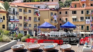 Una zona costera con varias embarcaciones de madera amarradas, un servicio de alquiler de botes pequeño y un edificio con balcones y banderas.