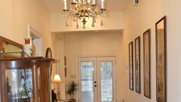 A hallway with wooden flooring, a chandelier, a glass display cabinet, and framed pictures on the wall. - "Henrietta's Magnolia" Located 2 1/2 blocks from historic downtown Breaux Bridge (Breaux Bridge)