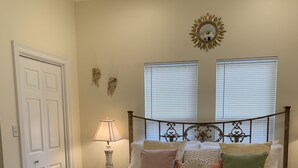 A bedroom with a large bed, a nightstand with a lamp, two windows with blinds, and a door. - "Henrietta's Magnolia" Located 2 1/2 blocks from historic downtown Breaux Bridge (Breaux Bridge)
