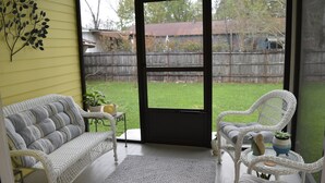 A covered patio with a sofa and chairs, a small table with a plant, and a view of a backyard through a glass door. - "Henrietta's Magnolia" Located 2 1/2 blocks from historic downtown Breaux Bridge (Breaux Bridge)
