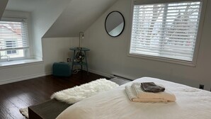Une chambre avec un grand lit, un tapis blanc et moelleux, un miroir rond accroché au mur et une fenêtre avec des stores.