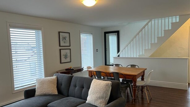 Un salon avec un canapé gris foncé, une table à manger en bois avec des chaises, et un escalier avec des rampes blanches.
