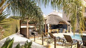 Un espace aménagé au bord de la piscine, avec des chaises longues, une structure à toit de chaume et une statue.