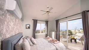 Une chambre à coucher avec un lit, un ventilateur de plafond, une fenêtre et un balcon équipé de chaises.