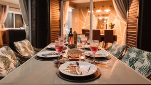Une table à manger dressée pour un repas, avec des chaises, des assiettes, des couverts, des verres et des bougies.