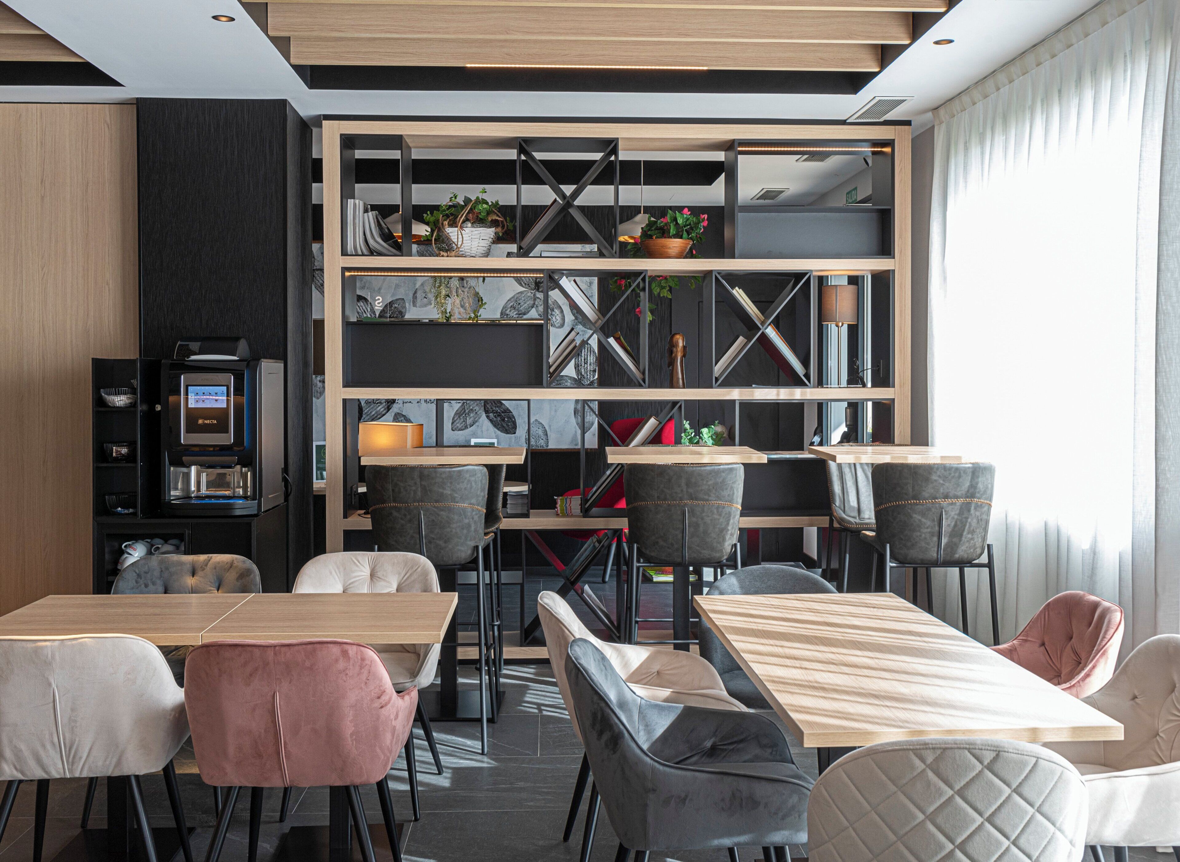 En moderne restaurant med træborde og stole, en kaffemaskine samt reoler med planter og dekorative genstande.