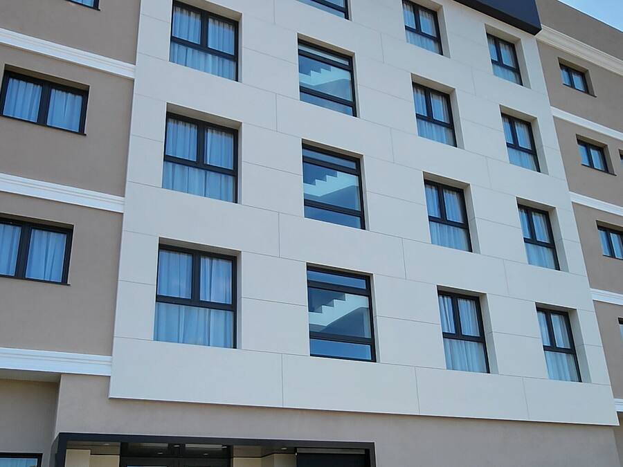 A multi-story hotel named "Plana Suites" with a modern facade, large windows, and a visible entrance with a door and potted plants.
