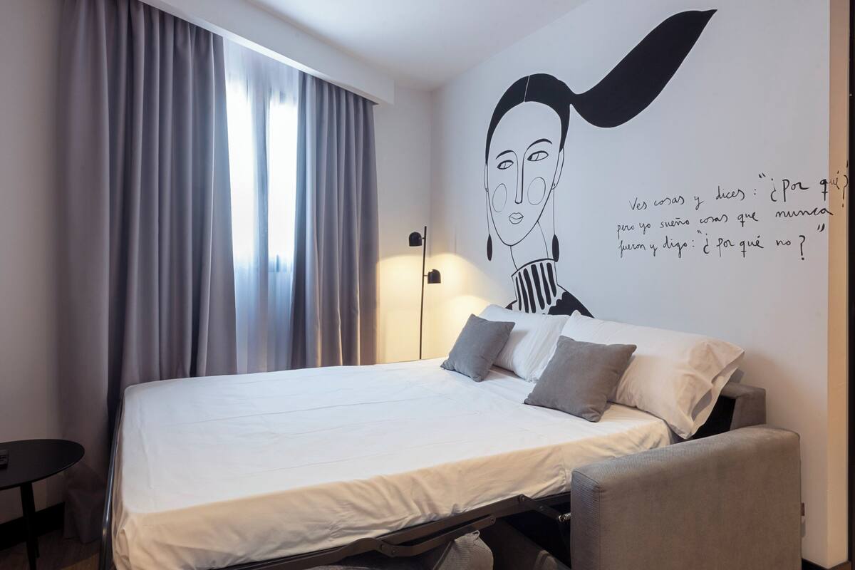 Una habitación de hotel moderna con una cama, un escritorio y un mural en la pared.