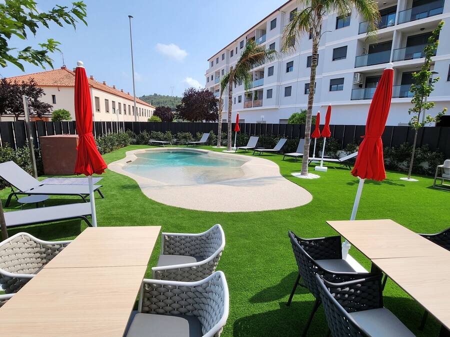 A pool area with artificial grass, lounge chairs, and red umbrellas.