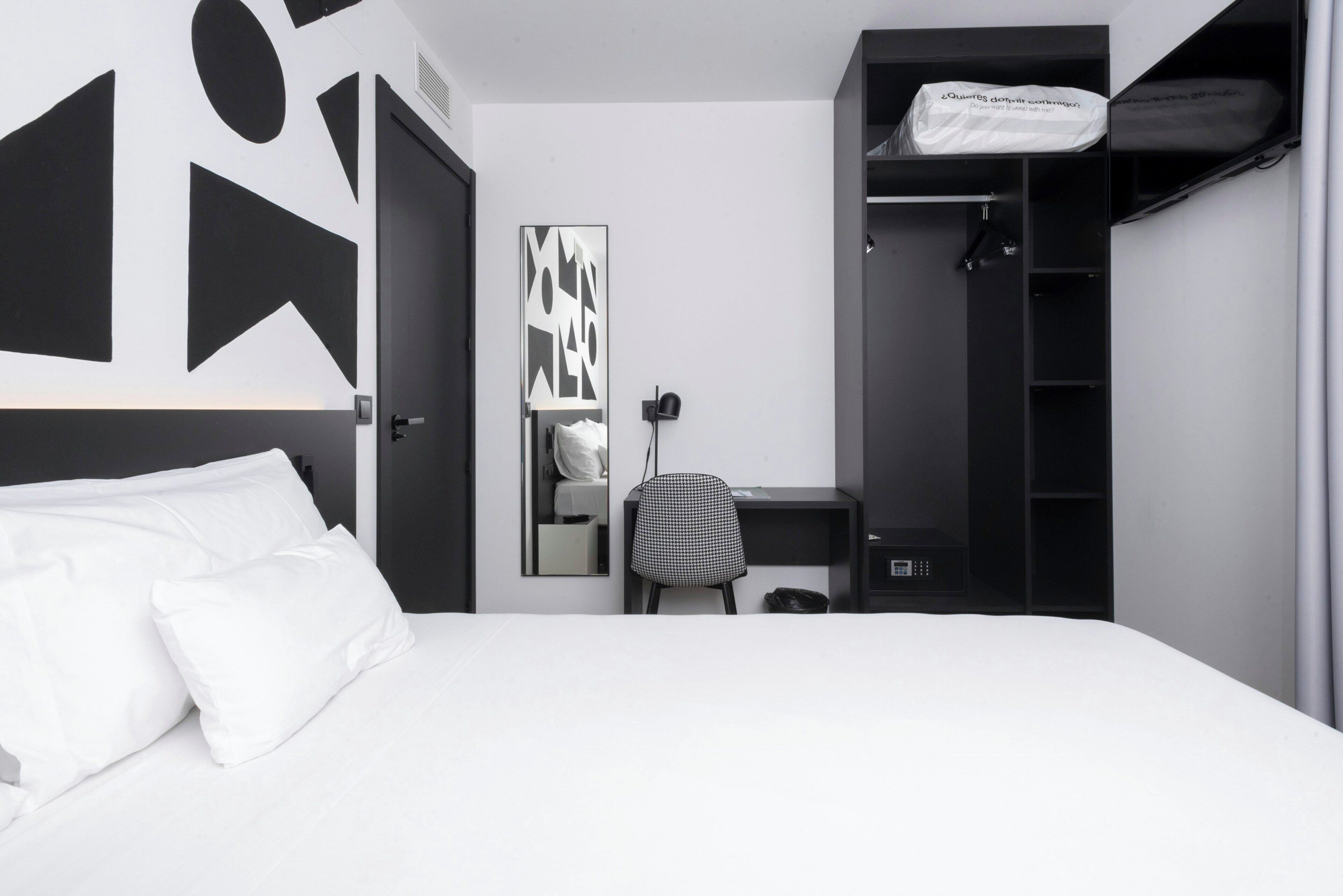 Ein Schlafzimmer mit Bett, Schreibtisch, Stuhl, Kleiderschrank und Spiegel.
