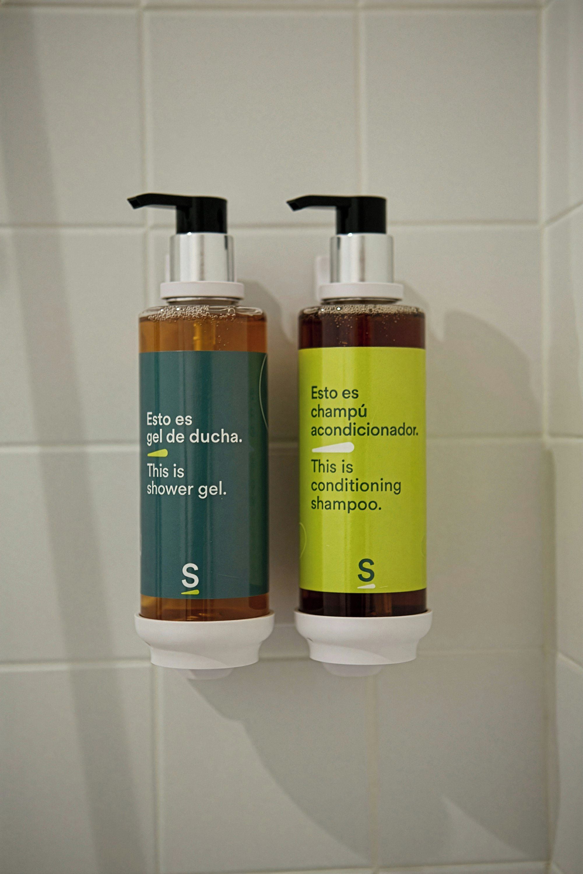 Two bottles of shower gel and conditioning shampoo on a tiled wall.