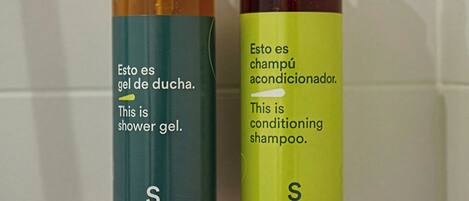 Two bottles of shower gel and conditioning shampoo on a tiled wall.
