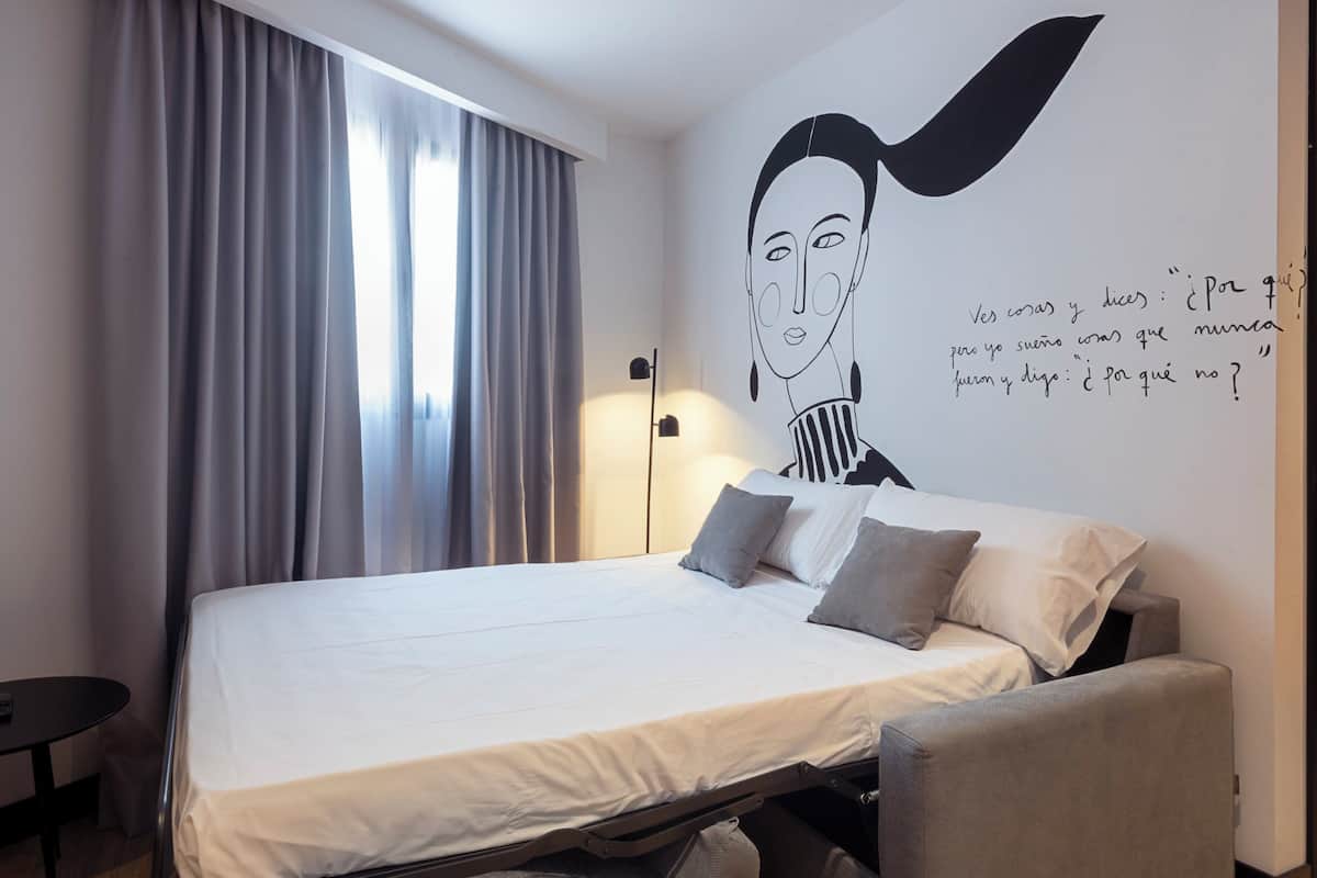 Quarto de hotel moderno com uma cama, uma escrivaninha e um mural na parede.