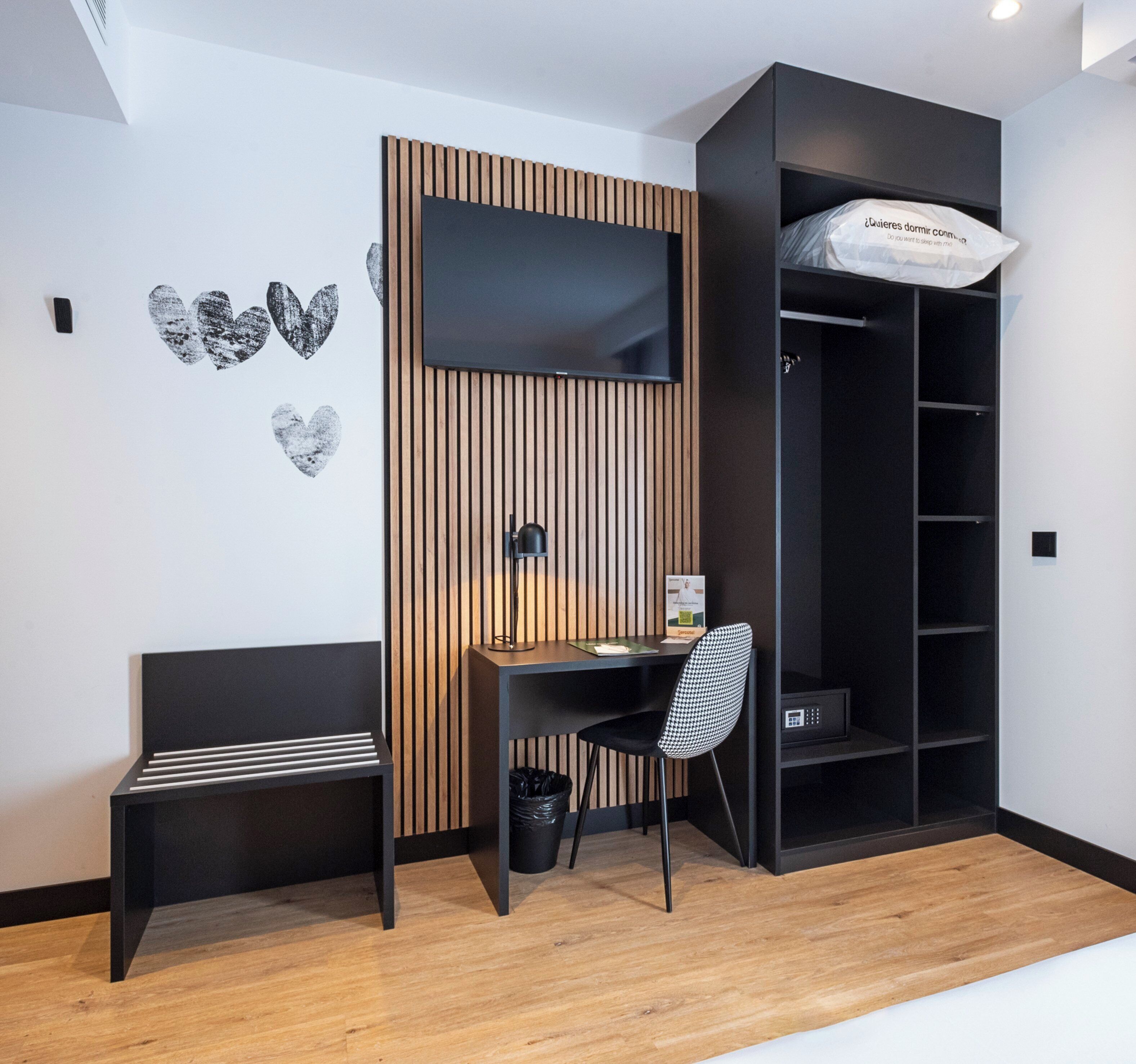 Ein modernes Zimmer mit einer Wand aus Holzlatten, einem Schreibtisch mit Stuhl, einem schwarzen Regalelement und einem schwarzen Mülleimer.