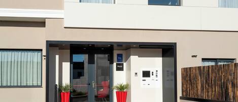 Entrada de un edificio moderno con puerta de cristal, sillas rojas y plantas en macetas.