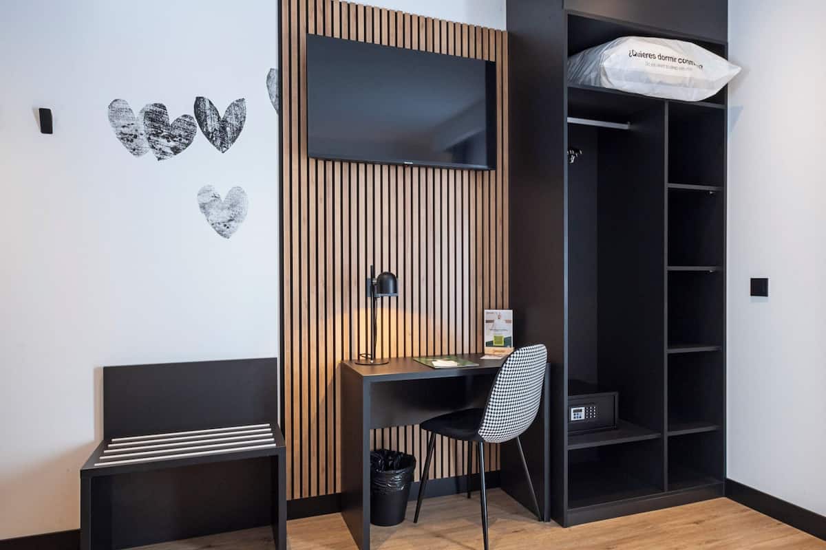Quarto moderno com parede de ripas de madeira, uma escrivaninha com cadeira, uma estante preta e um cesto de lixo preto.