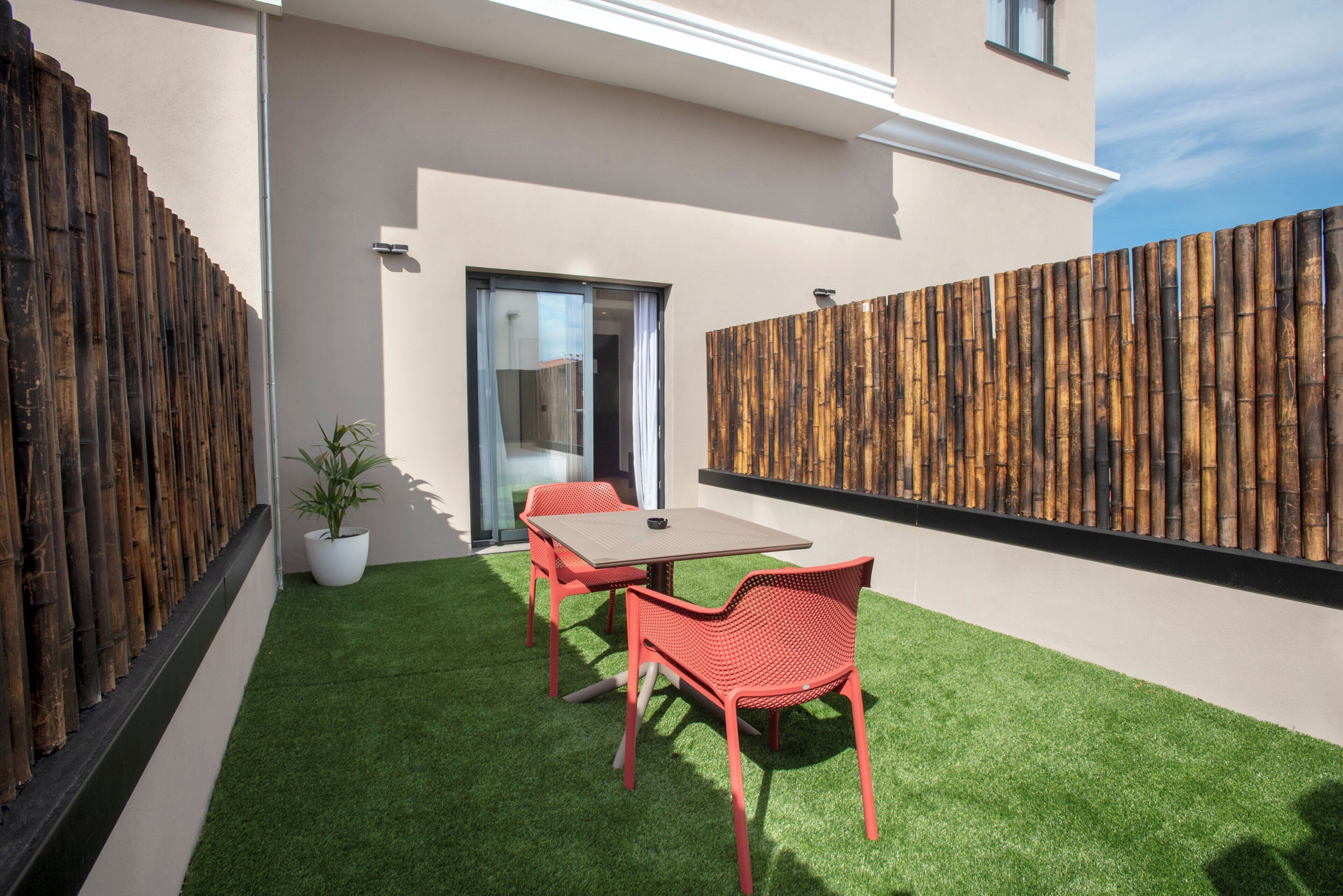 A modern outdoor patio with a table and chairs, a potted plant, and a wooden fence.